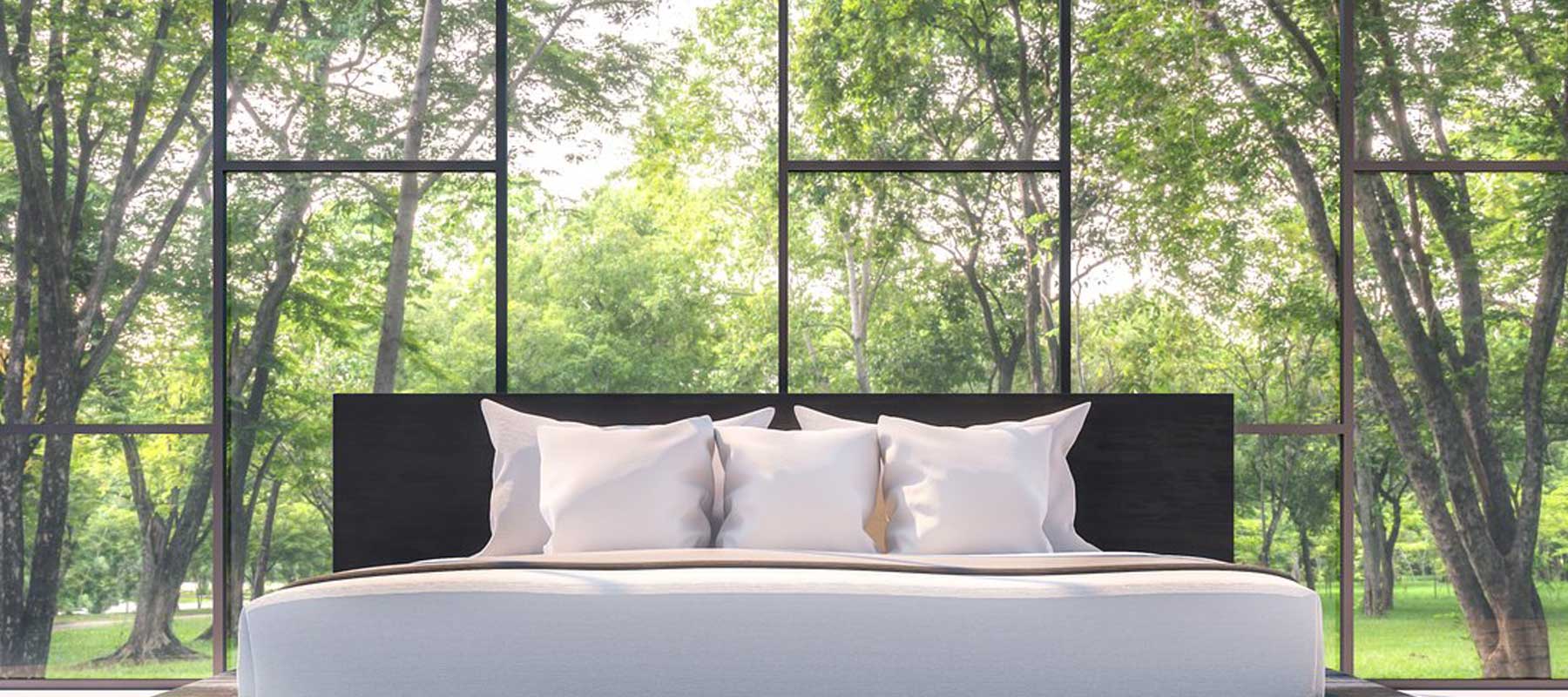 Oversized bed in front of big windows that look out into the trees. 
