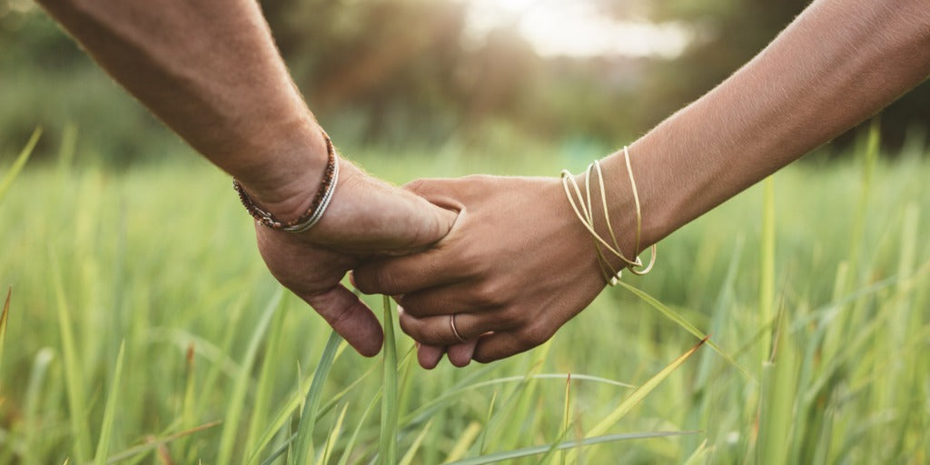 Couple holding hands in field of grass. 